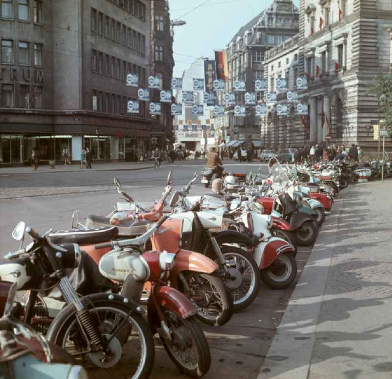 Motorräder / Mopeds u.a. vom Typ Spatz, Schwalbe, MZ, Simson usw. stehen nebeneinander am Straßenrand. In der Fußgängerzone wird für die Ausstellungen der Herbstmesse geworben.