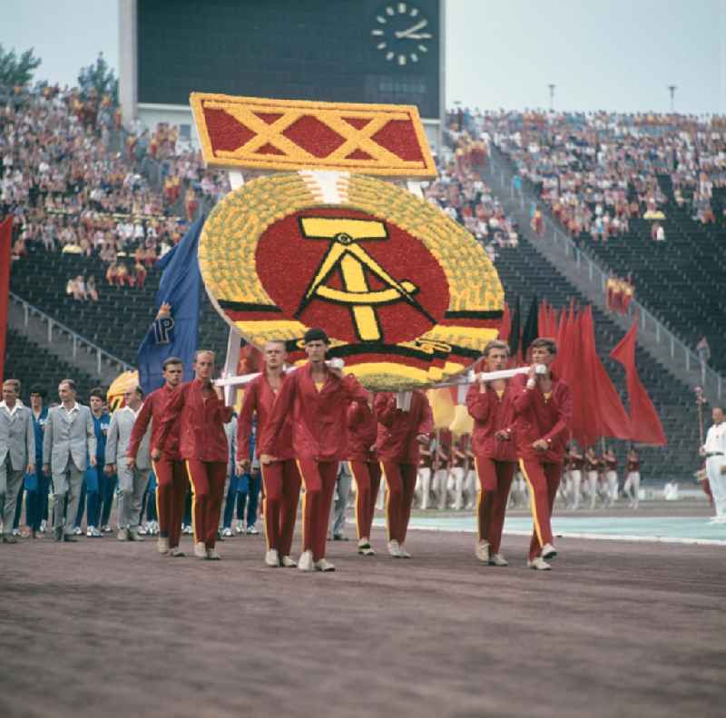Zur Generalprobe der Sportschau zum V. Turn- und Sportfest der DDR vom 24. bis 27.7.1969 in Leipzig tragen die Teilnehmer das DDR-Emblem auf ihren Schultern in das Leipziger Zentralstadion. Zugleich wird an den 2