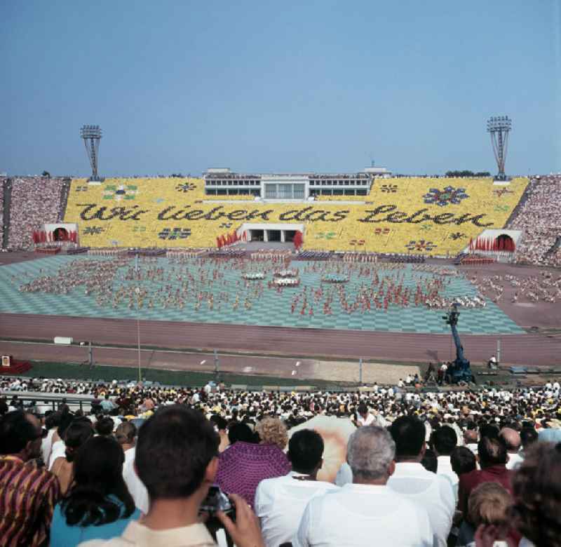 Für die Sportschau zum V. Turn- und Sportfest der DDR vom 24. bis 27.7.1969 in Leipzig gestalten die Teilnehmer im Leipziger Zentralstadion eine Veranstaltung mit Tribünenbildern und Aktionen. Die Losung lautet: 'Wir lieben das Leben'.