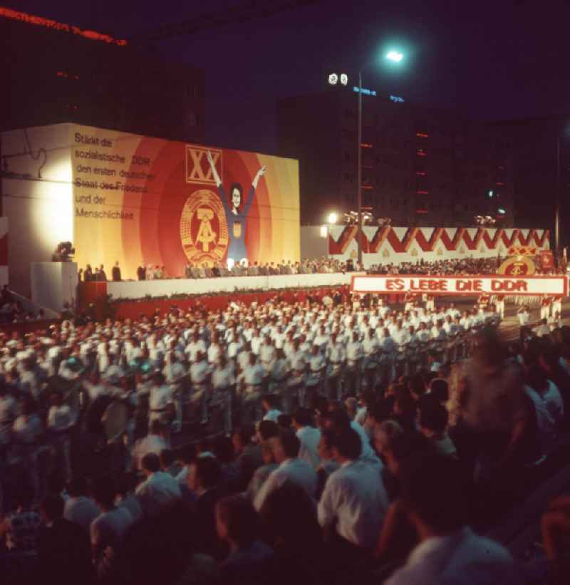 Nächtlicher Aufmarsch von Sportlern und Teilnehmern am V. Turn- und Sportfest der DDR vom 24. bis 27.7.1969 vor der Ehrentribüne am Georgiring in Leipzig. Hinter der Tribüne eine Losung zum 2