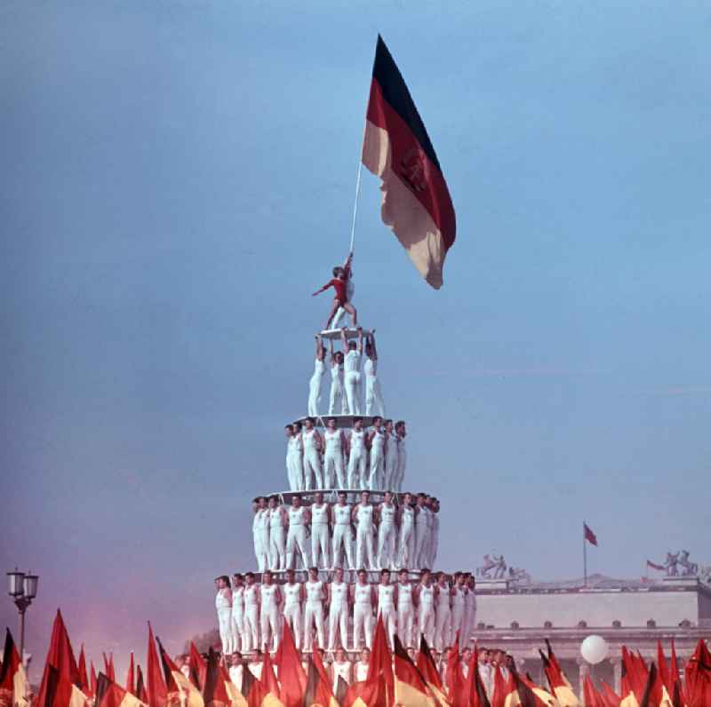 Sportler bauen eine Pyramide aus Menschen auf der Festwiese des Leipziger Zentralstadions beim V. Turn- und Sportfestes der DDR vom 24. bis 27.7.1969. Das Turnerpaar auf der Spitze der Pyramide hält die Fahne der DDR in die Höhe.