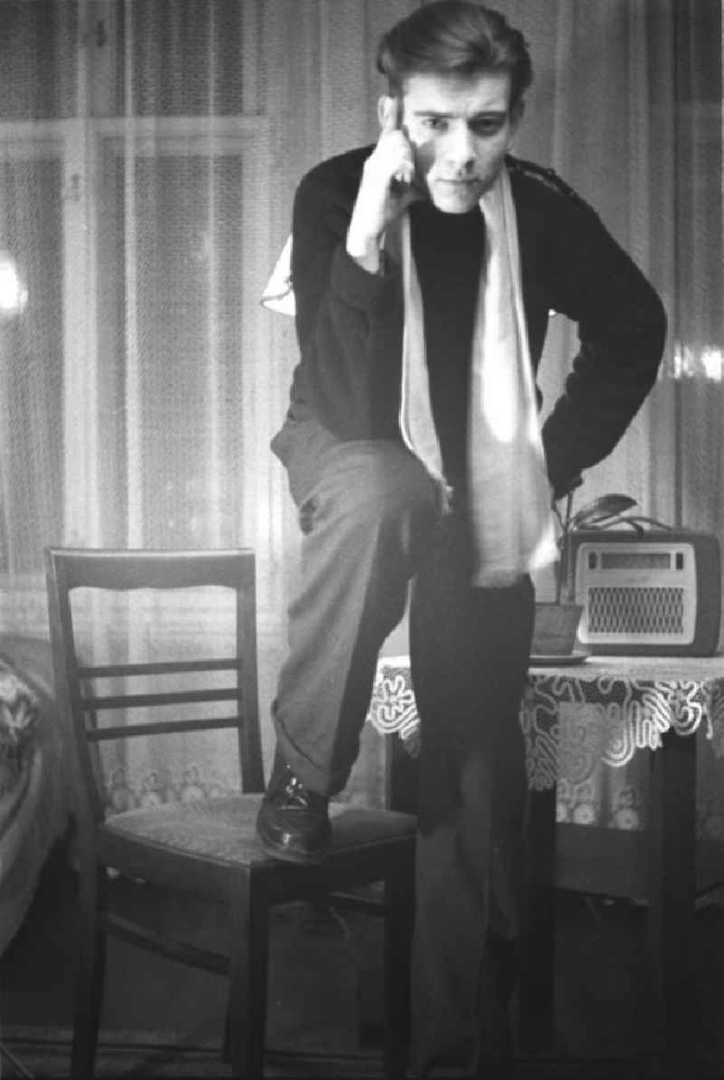 Frühes Selbstportrait des Fotografen Klaus Morgenstern. Morgenstern, lässig bis elegant gekleidet, posiert mit einem Stuhl. Auf einem beistehenden Tisch ein Radiogerät der 5