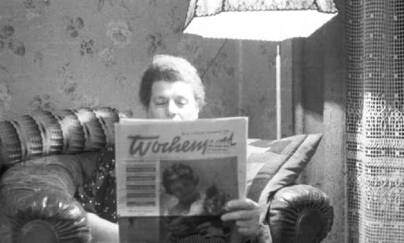 Eine Frau liest im Wohnzimmer auf einem Sessel eine Ausgabe der Wochenpost. Das Titelbild zeigt ein junges Mädchen mit einem Löwenjungen im Arm. Bestmögliche Qualität nach Vorlage!