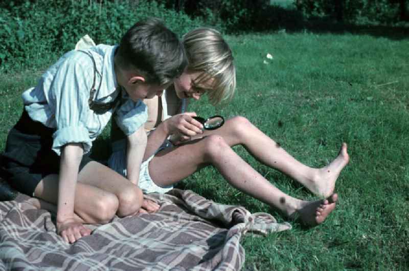 Jungs experimentieren mit einer Lupe auf einer Decke im Freibad. Boys experiment with a magnifier on a blanket in the open-air bath.