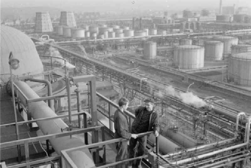 Blick auf die Raffinerie VEB Mineralölwerk Lützkendorf. Arbeiter stehen im Vordergrund zusammen.