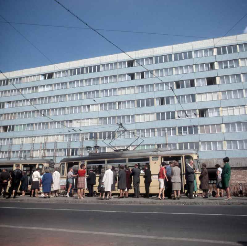Passanten stehen an einer Straßenbahn-Haltestelle im Zentrum von Magdeburg. Die Magdeburger Innenstadt war während des Zweiten Weltkrieges zum großen Teil zerstört worden. Die meisten beschädigten Gebäude wurden in der DDR abgerissen und durch Plattenbauten ersetzt, hier das Bürogebäude der s.g. 'Blaue Bock' im Hintergrund.