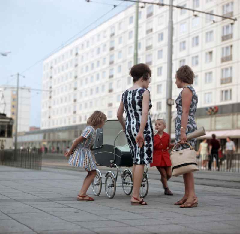 Zwei Frauen mit ihren Kindern unterhalten sich auf der Karl-Marx-Straße, heute Breiter Weg, in Magedeburg. Die Magdeburger Innenstadt war während des Zweiten Weltkrieges zum großen Teil zerstört worden. Die meisten beschädigten Gebäude wurden in der DDR abgerissen und durch Plattenbauten ersetzt.