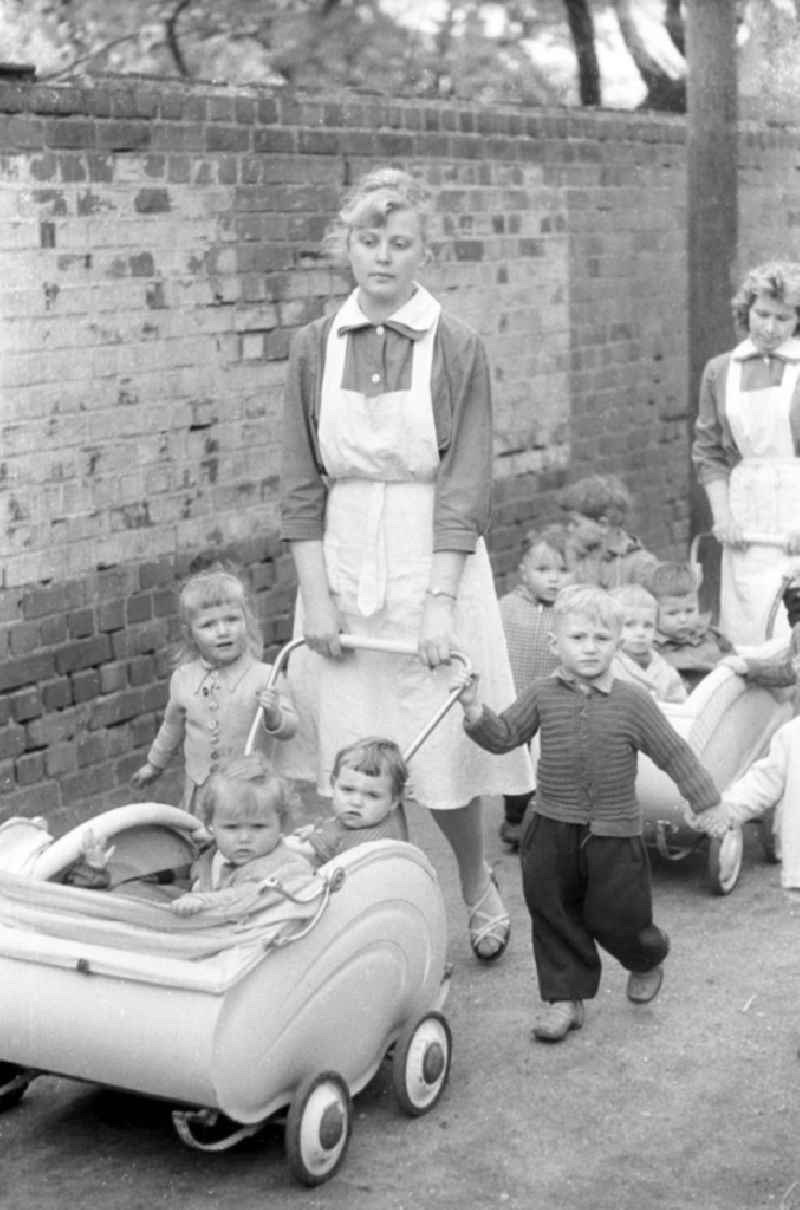 Eine Erzieherin mit Kindern und Kinderwagen im Stil der frühen 196