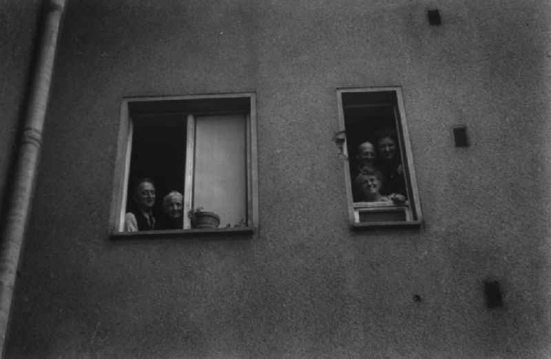 Anwohner eines Mehrfamilienhauses gucken aus dem Fenster. Residents of an apartment building look out of the window.