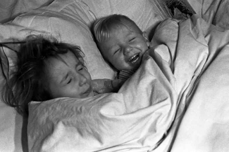 Two small children lie laughing in the bed of the parents and look to themselves children's books in in Merseburg in the federal state Saxony-Anhalt in Germany