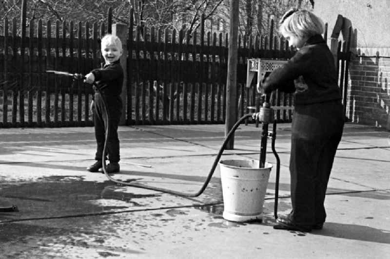Two children play in the inner courtyard with a water hose in Merseburg in the federal state Saxony-Anhalt in Germany