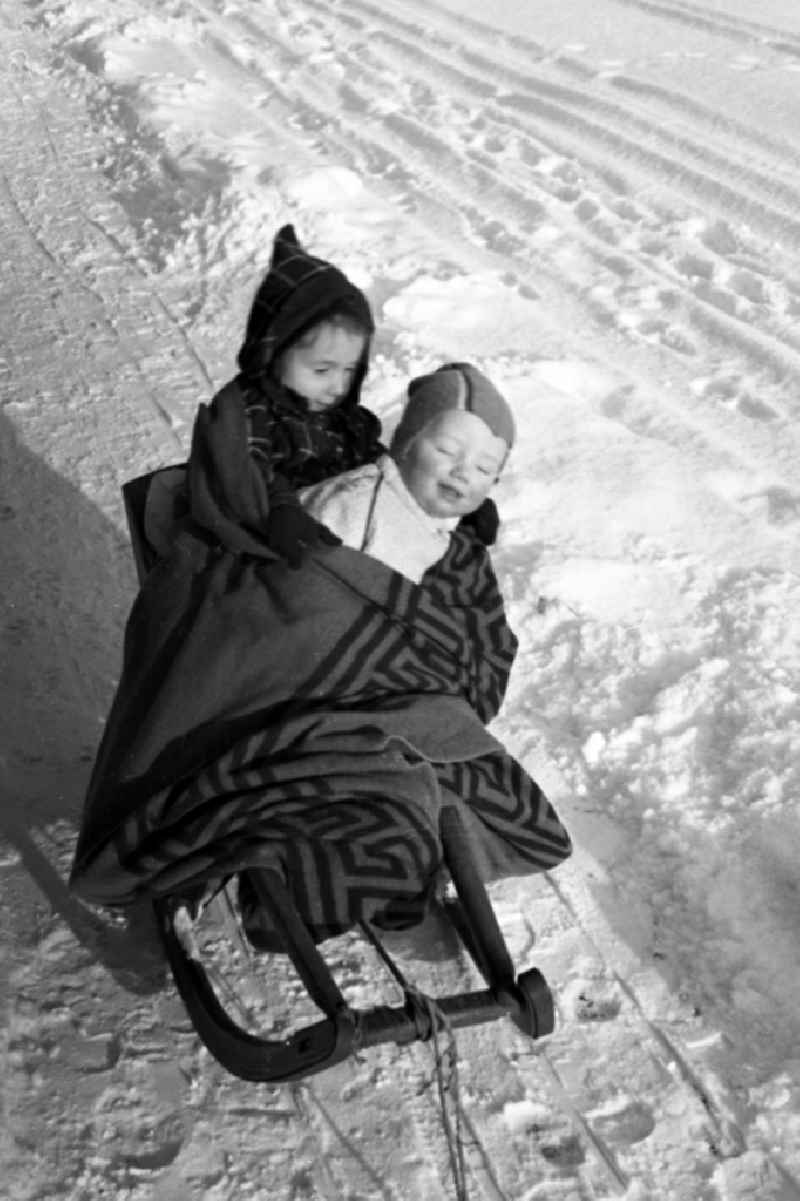 Two children lie, muffled in a thick cover, on a sledge in Merseburg in the federal state Saxony-Anhalt in Germany