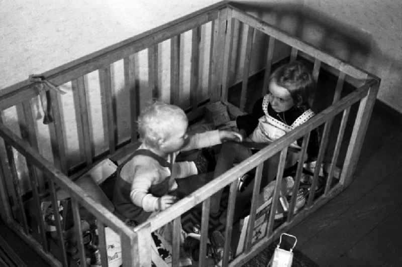 The big sister plays with her smaller brother in the playpen in Merseburg in the federal state Saxony-Anhalt in Germany