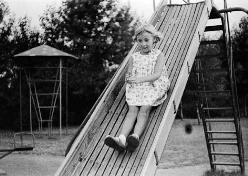 A small girl slides on a children's slide on a playground in Merseburg in the federal state Saxony-Anhalt in the area of the former GDR, German democratic republic