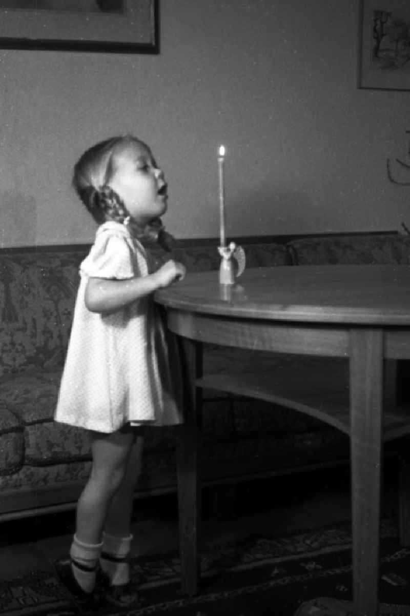 A small girl with plaits tries to blow out a candle which stands on the table, in Merseburg in the federal state Saxony-Anhalt in Germany