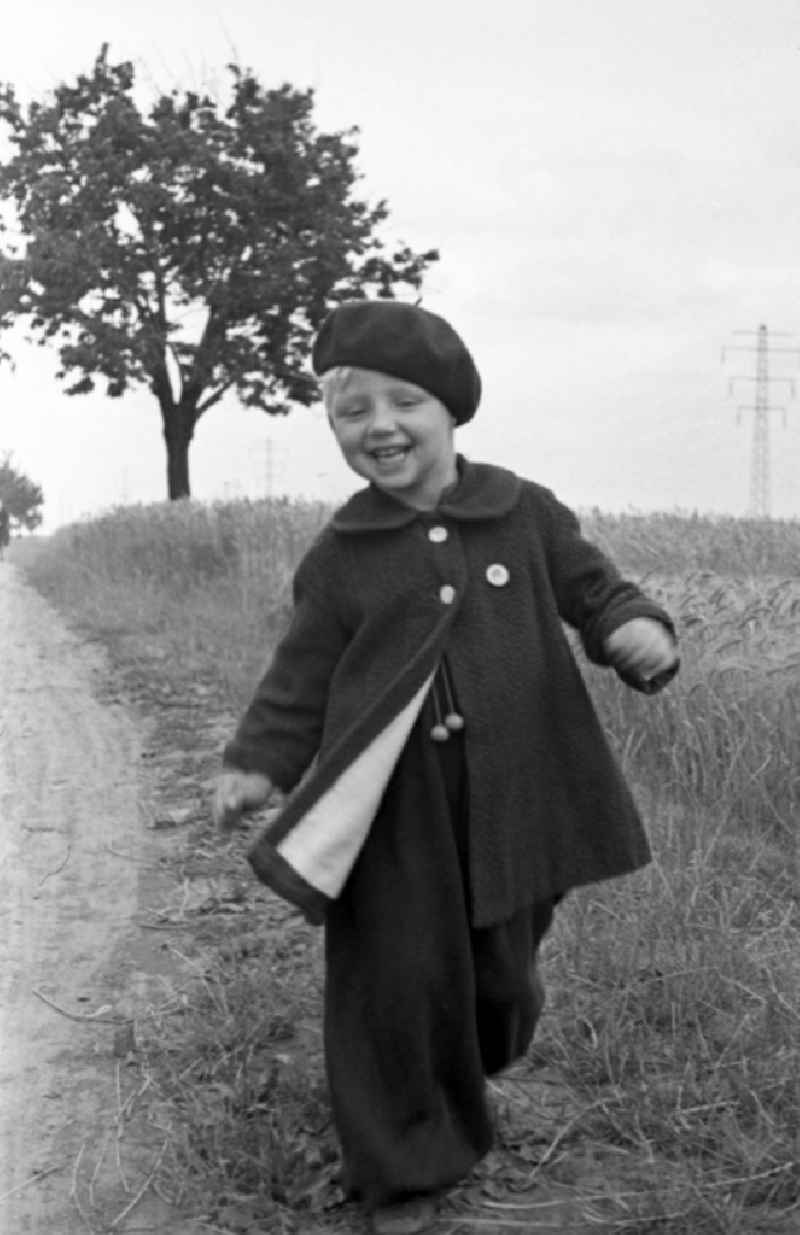 A small child in baggy trousers and with beret runs on a country lane in Merseburg in the federal state Saxony-Anhalt in the area of the former GDR, German democratic republic