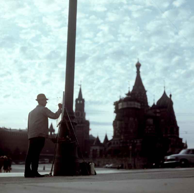 Ein Maler steht im Gegenlicht an seiner Staffelei und malt den Spasski Turm (l) und die Basilius-Kathedrale (r) am Roten Platz in Moskau.