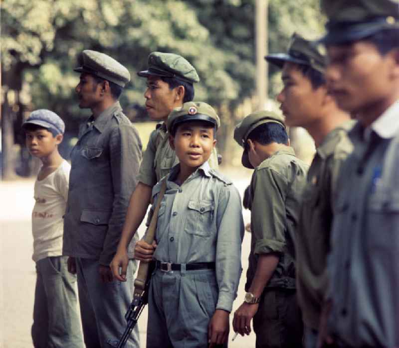 Soldaten der laotischen Armee, darunter auch Kinder, in der Demokratischen Volksrepublik Laos. Erst ein Jahr zuvor, am 2. Dezember 1975, war durch die kommunistisch geprägten Kräfte die Volksrepublik Laos ausgerufen worden. Die politische und wirtschaftliche Situation blieb aber auch in den Folgejahren unsicher und instabil. Immer wieder kam es zu Rebellionen aus dem Hinterland, die mit Hilfe der Armee und ausländischer, v.a. vietnamesischer, Unterstützung gewaltsam niedergeschlagen wurden.