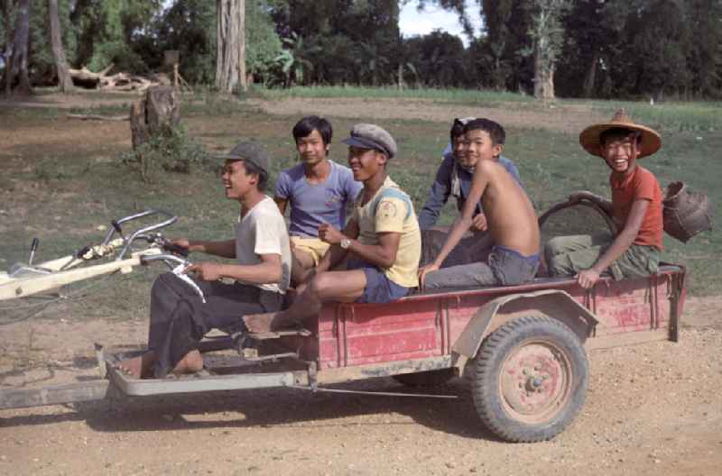 Auf dem Weg zur Feldarbeit amüsieren sich junge Männer auf dem Anhänger eines elektrischen Karrens in der Demokratischen Volksrepublik Laos.