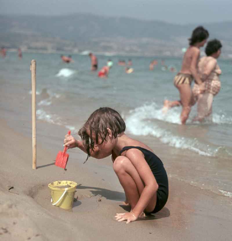 Ein Mädchen spielt mit dem nassen Sand am Strand von Nessebar am Schwarzen Meer in der Volksrepublik Bulgarien. Reisen in das Ausland war den DDR-Bürgern nur in die befreundeten sozialistischen Länder erlaubt, für Bulgarien erfolgte in der Regel die Erteilung einer Reisegenehmigung.