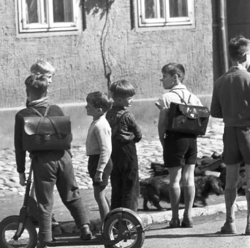 Kinder / ein Kind mit einem Roller auf einer Straße. Einige Jungen mit Schulranzen / Schultasche. Orlamünde gehört zum heutigen Saale-Holzland-Kreis und liegt an der Mündung der Orla in die Saale. Bestmögliche Qualität nach Vorlage!