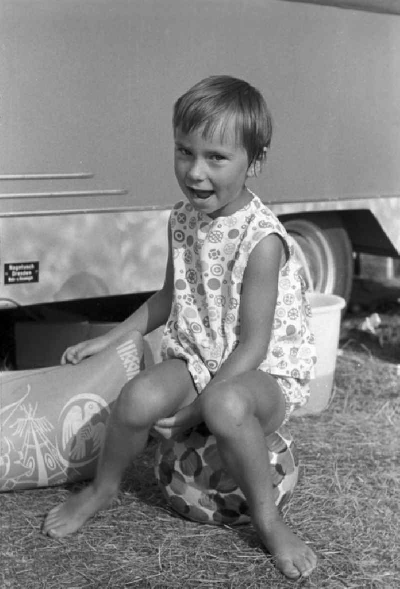 A small child sits on a ball, laughing mischievously in Brandenburg. Family camping holidays at Rottstielfließ on Tornowsee in Brandenburg