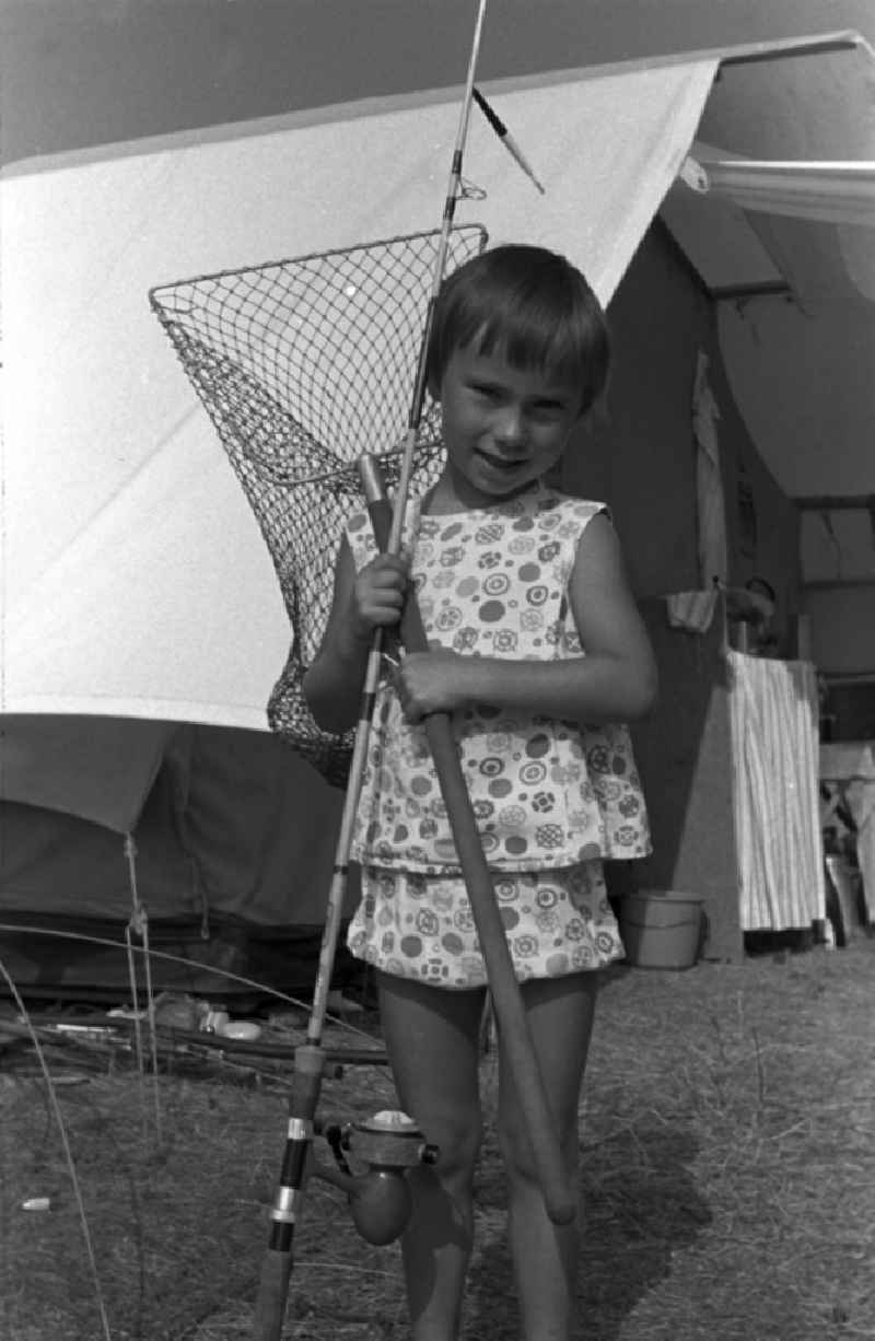 A little girl with fishing rod and landing net in front of a tent in Brandenburg