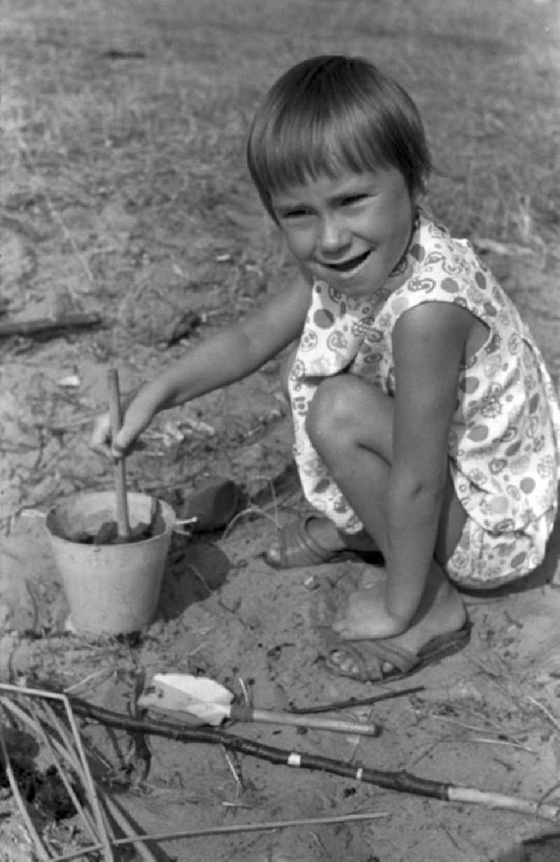 A small child playing with a bucket in the sand in Brandenburg. Family camping holidays at Rottstielfließ on Tornowsee in Brandenburg