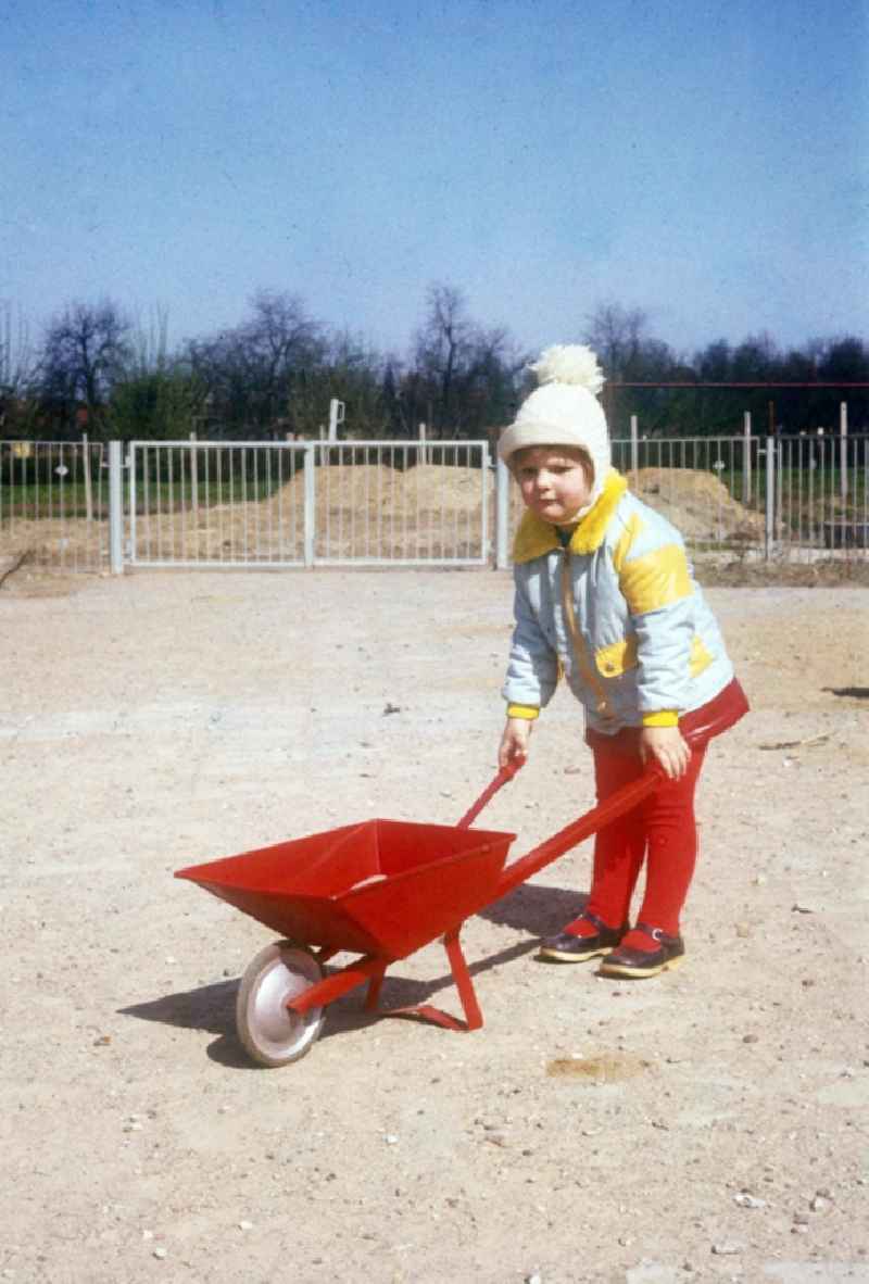 Child with a red barrow and poodle's cap in Neustrelitz in the federal state Mecklenburg-West Pomerania in the area of the former GDR, German democratic republic