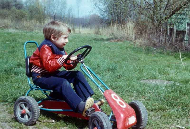 A child sits on a pedal car Kettcar in Neustrelitz in the federal state Mecklenburg-West Pomerania in the area of the former GDR, German democratic republic