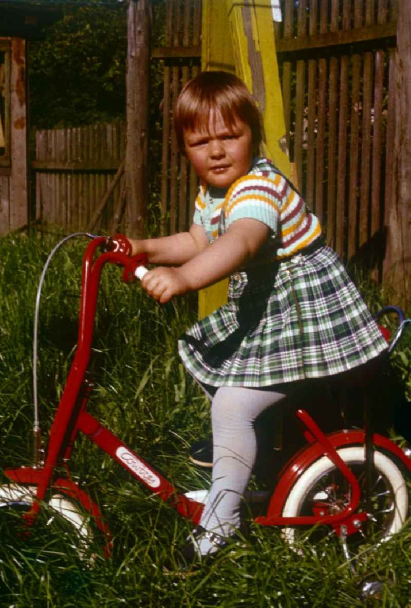 A girl in the checked rock on a red children's bicycle of the brand Cowboy in Neustrelitz in the federal state Mecklenburg-West Pomerania in the area of the former GDR, German democratic republic