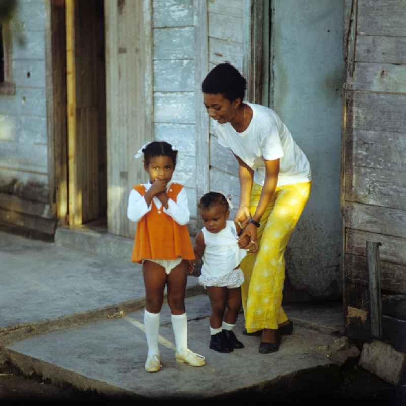 Eine Frau mit ihren zwei Kindern vor dem Eingang ihrer ärmlich wirkenden Behausung in einer Wohnsiedlung in der kubanischen Hafenstadt Nuevitas. Woman with children on the front door.