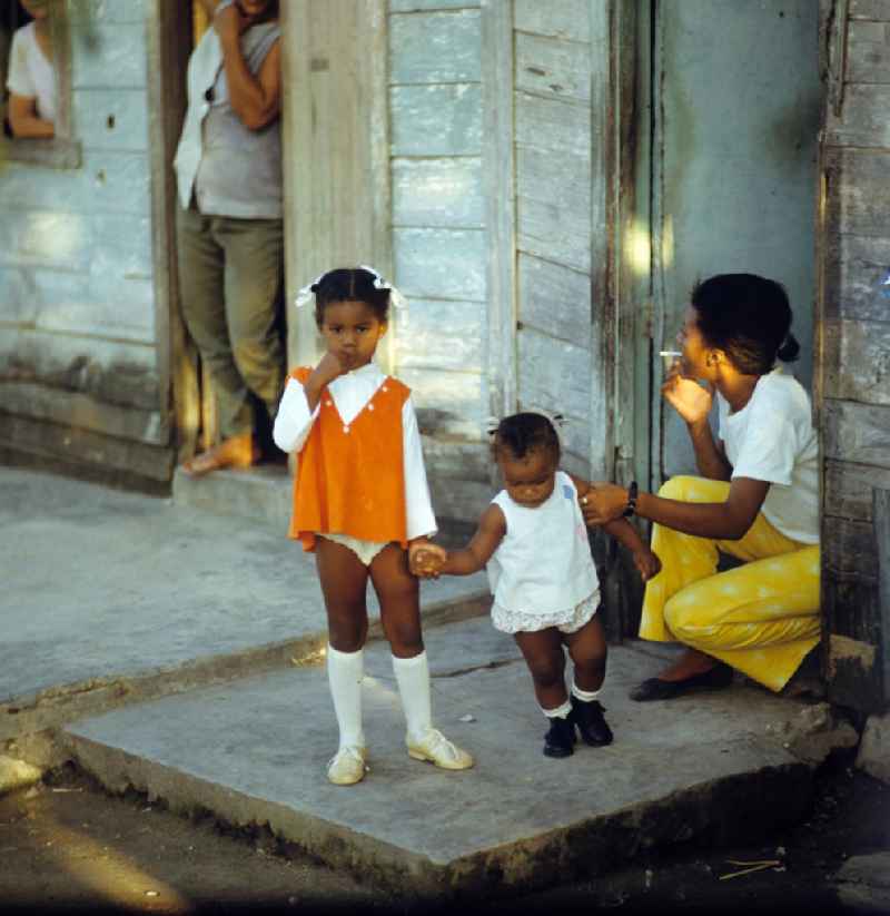 Eine Frau mit ihren zwei Kindern vor dem Eingang ihrer ärmlich wirkenden Behausung in einer Wohnsiedlung in der kubanischen Hafenstadt Nuevitas. Woman with children on the front door.