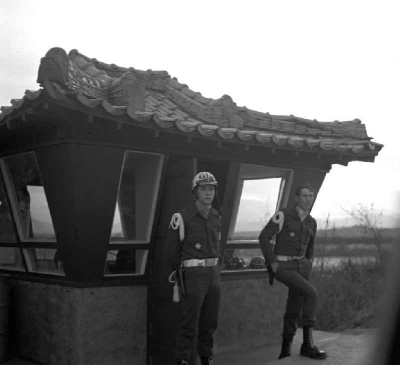 Zur JSA (Joint Security Area) gehörende Angehörige der US-Army stehen an der Ausfahrt von Panmunjeom. Panmunjeom ist eine militärische Siedlung in der entmilitarisierten Zone zwischen Nord- und Südkorea und seit dem Waffenstillstandsabkommen 1953 das Hauptquartier der Military Armistice Commission (MAC), die die Einhaltung des Waffenstillstands überwacht. Seit den Gesprächen des Waffenstillstandskomitees des Roten Kreuzes im Herbst 1971 wurden in Panmunjeom Gespräche zwischen Nord- und Südkorea geführt, wobei vor allem das Thema der Familienzusammenführungen bzw. -treffen im Mittelpunkt stand. Es ist die einzige zollähnliche 'offene' Grenzstelle, wo ohne Grenzübertretung am selben Tisch Verhandlungen und Gespräche stattfinden konnten.