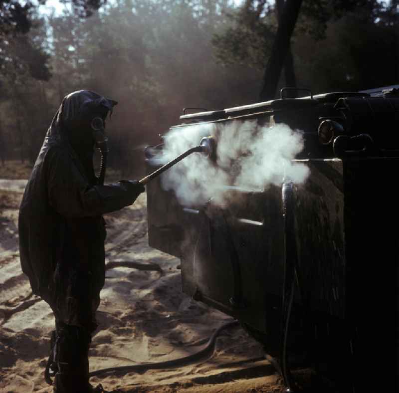 Manöverübung der NVA-Truppen der chemischen Abwehr (ABC-Abwehr) in Peenemünde. Ein Soldat in Schutzanzug (ABC-Anzug, Gummianzug) mit Gasmaske bei der Entaktivierung (Dekontaminierung, Dekontamination) eines kontaminierten Fahrzeugs.