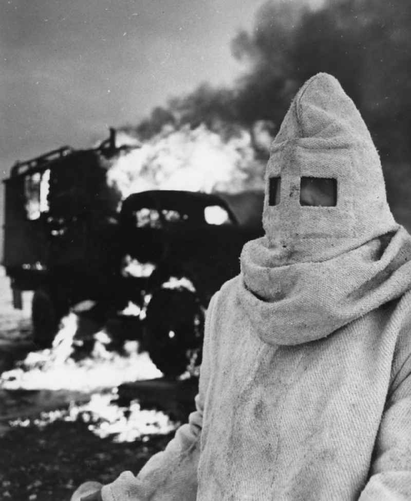Maneuver exercise of NVA troops of the chemical defense (NBC) in Peenemuende in Mecklenburg-Vorpommern. In the foreground a soldier in a asbestos and fire resistant protective clothing. In the background burning objects
