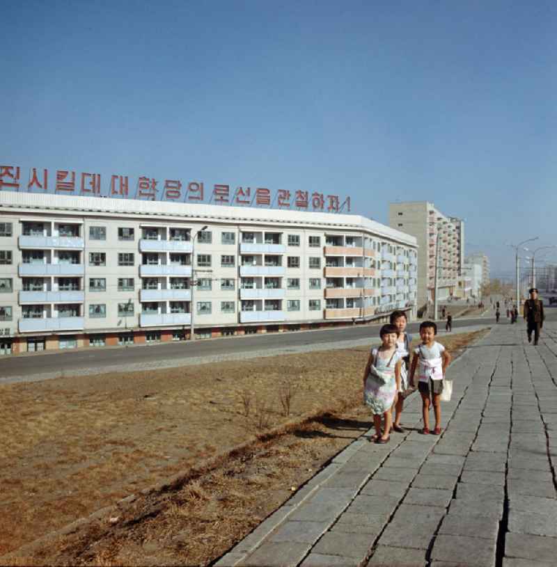 Kinder spielen auf einer Straße in Pjöngjang, der Hauptstadt der Koreanischen Demokratischen Volksrepublik (KDVR). Im Hintergrund Plattenbauten im sozialistischen Stil mit Propaganda auf dem Hausdach. Die nordkoreanische Hauptstadt war nach der Zerstörung im Koreakrieg vor allem mit Unterstützung der Sowjetunion in den 50er und 6
