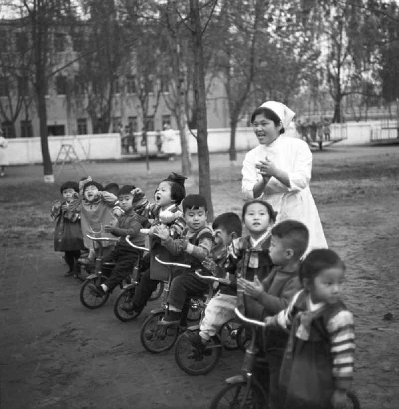 Kinder stehen mit ihren Dreirädern in einer Reihe auf dem Spielplatz in einem Kindergarten in Pjöngjang, der Hauptstadt der Koreanischen Demokratischen Volksrepublik KDVR - Nordkorea / Democratic People's Republic of Korea DPRK - North Korea.