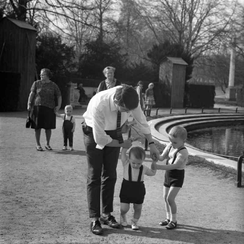 Ein Vater unterstützt seinen jüngeren Sohn bei dessen Gehversuchen in einem Park in Potsdam. A father supports his younger son at his first attempts at walking in a park in Potsdam.