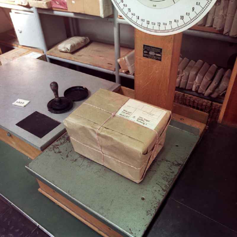 Ein Paket wird auf einer Paketwaage in einer Filiale in Potsdam abgewogen. Im Hintergrund Regale mit Paketen und Päckchen.