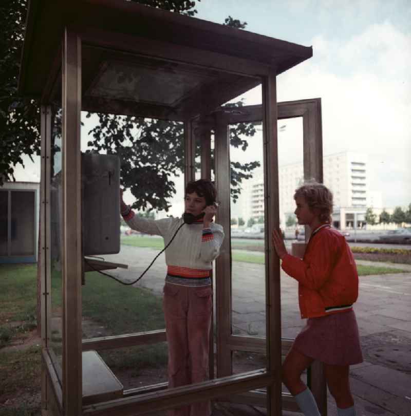 Zwei Mädchen benutzen ein modernes Telefonhäuschen / Telefonzelle in Potsdam.