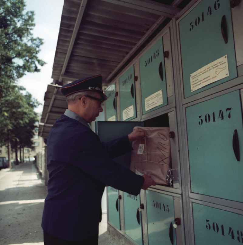Ein Briefträger stellt ein Paket zu in den Briefkasten eines Wohnhauses.