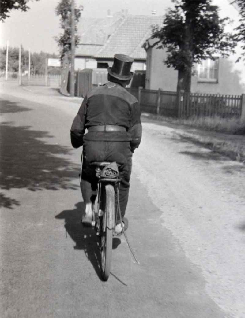 Chimney sweep in typical working clothes with equipment of his craft on a bike in Prerow in the state Mecklenburg-Western Pomerania on the territory of the former GDR, German Democratic Republic