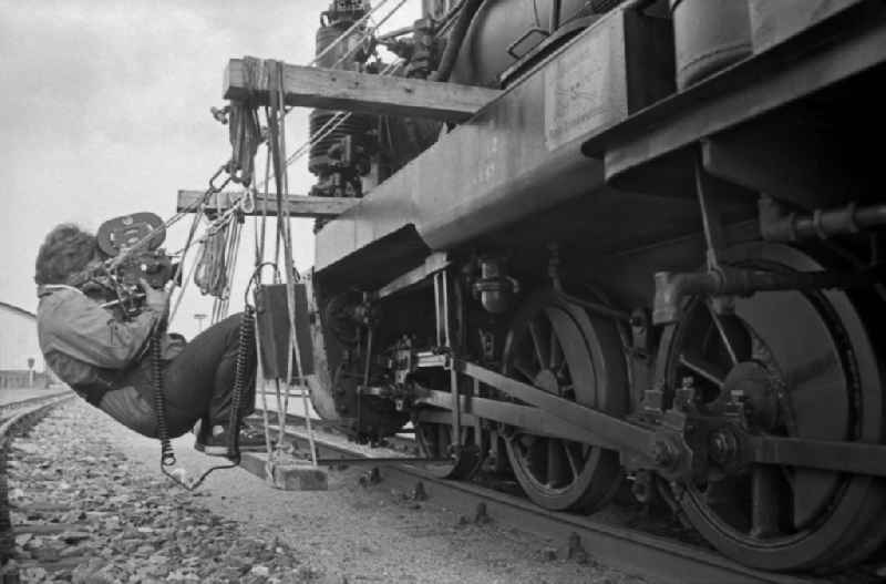 Cameraman filming the track rod of the chassis of a steam locomotive of the Ruegensche Baederbahn - Rasender Roland train on the station premises of the Deutsche Reichsbahn narrow-gauge railway in Putbus, Mecklenburg-Western Pomerania on the territory of the former GDR, German Democratic Republic