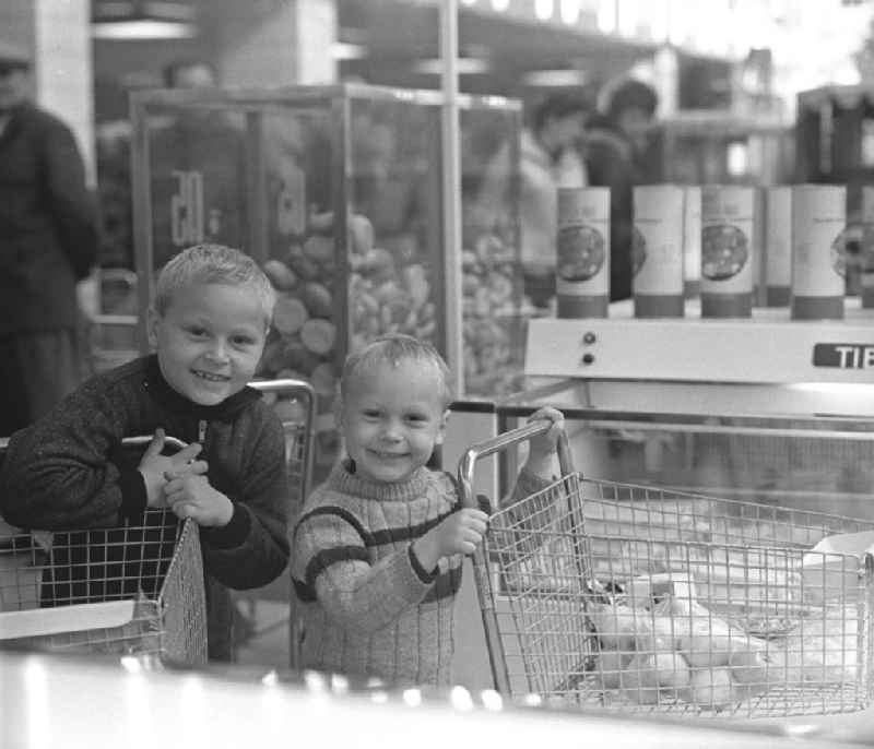Jungen mit Einkaufswagen lächeln in die Kamera in der HO Kaufhalle im Ortsteil Lütten Klein in Rostock. Eröffnung am 04.