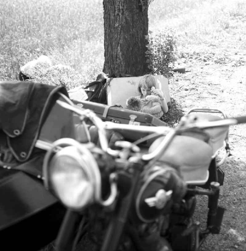 Motorradpanne auf der Landstraße - während die Eltern sich um die Reparatur des Motorrades kümmern, genießt ein Mädchen die (Zwangs-)Pause unter einem Baum.
