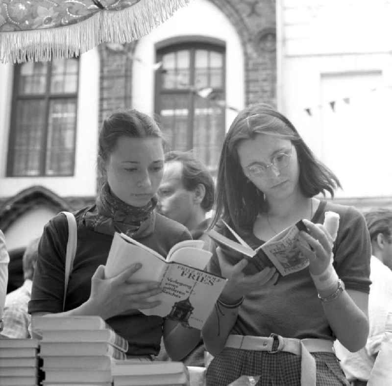 Besucherinnen blättern in einem Buch an einem Buchstand des Schriftstellerbasars in Rostock.