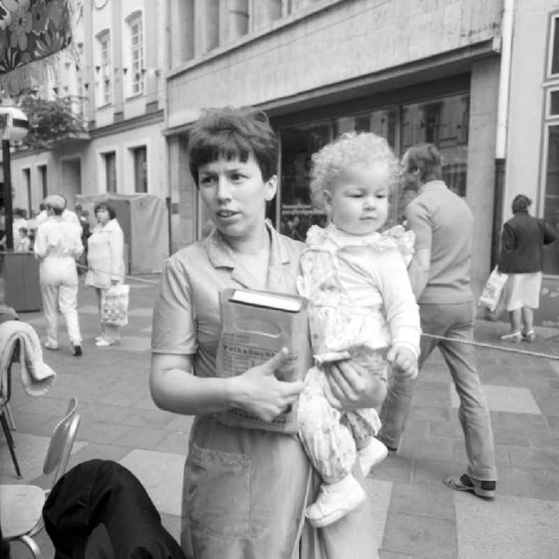 Eine Frau steht mit einem Kind auf dem Arm auf dem Schriftstellerbasar in Rostock.