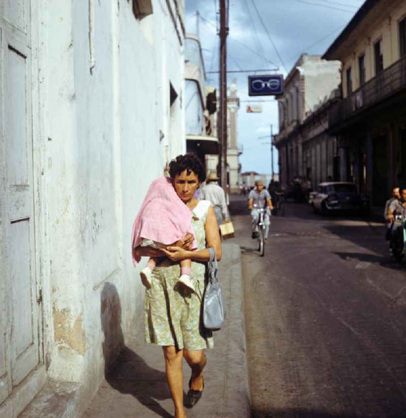 Straßenszene in Santa Clara in Kuba - eine Mutter läuft mit ihrem kleinen Kind auf dem Arm die Straße entlang. Street scene in Santa Clara - Cuba.