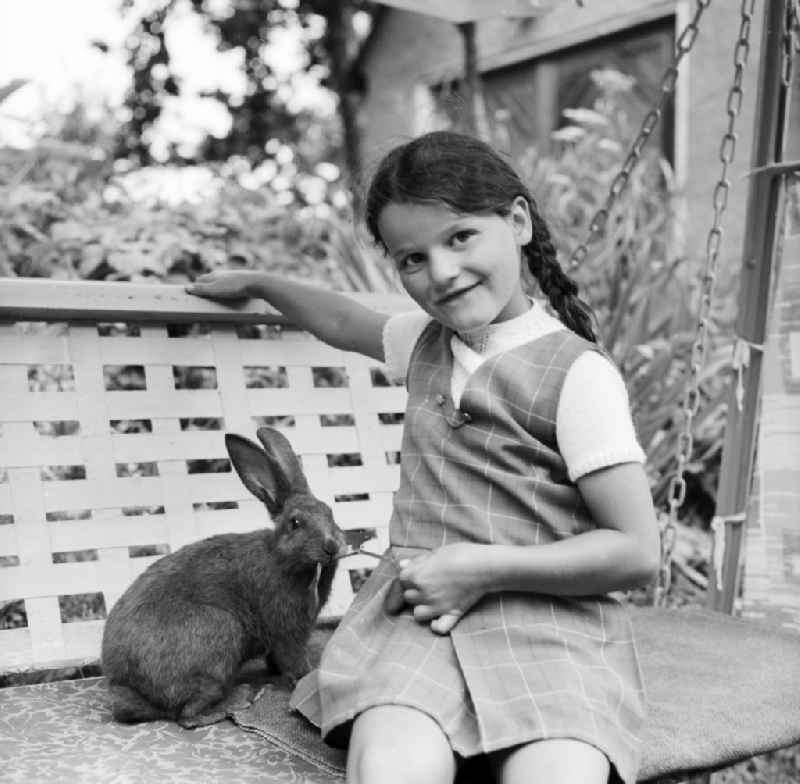 Girl sits with a rabbit of a garden swing in Scheibenberg in the federal state Saxony in the area of the former GDR, German democratic republic
